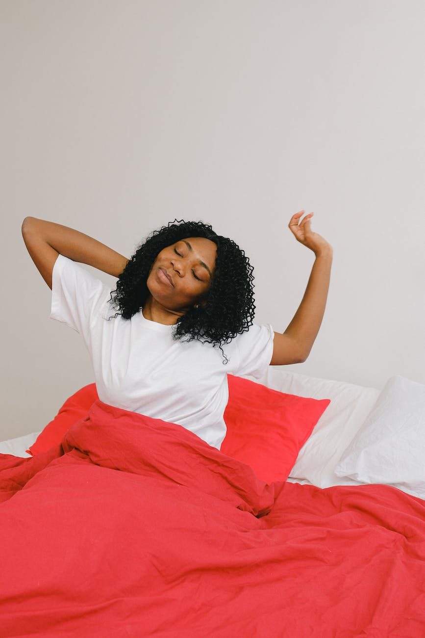 cheerful black woman waking up in bed with red blanket